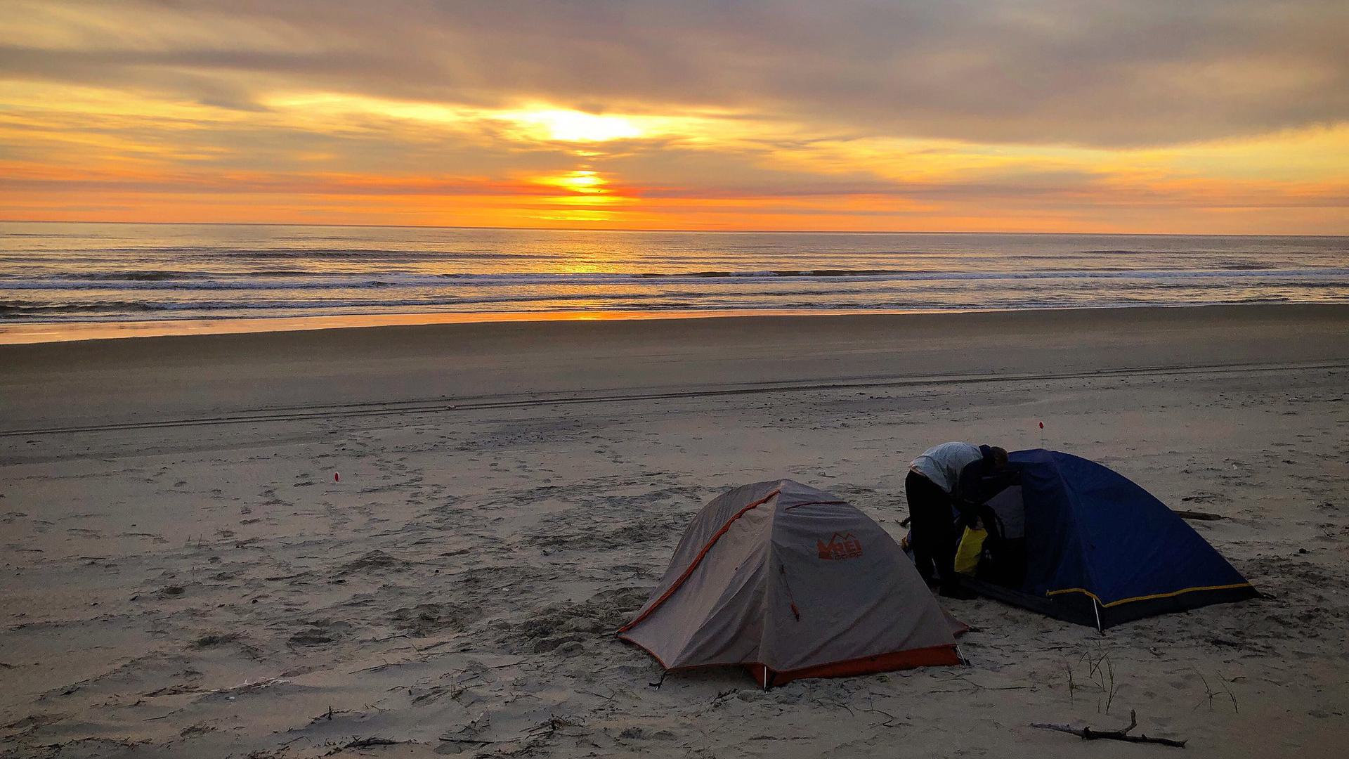 two tents on a beach at sunset
