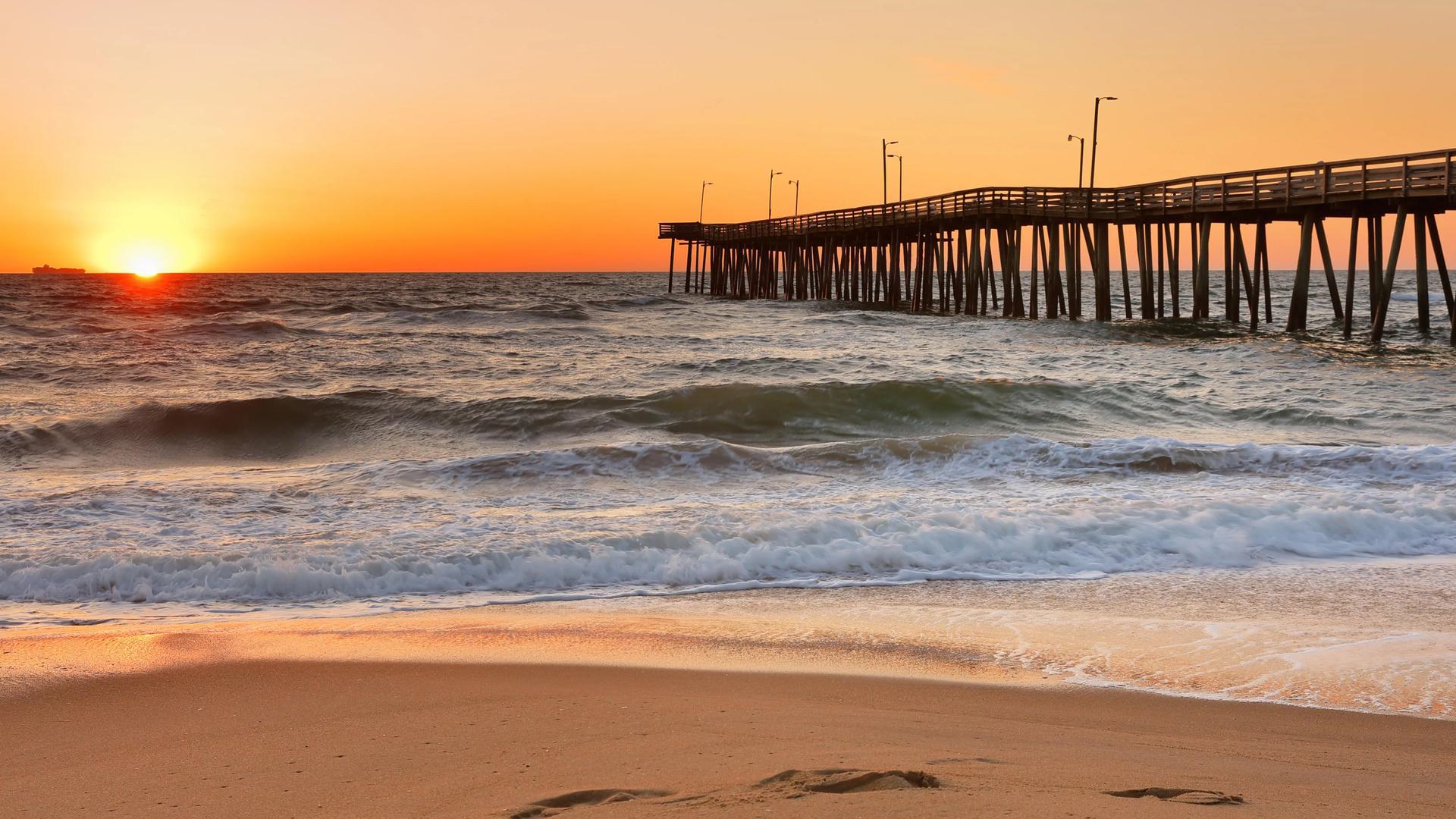a photo of a beach at sunset with water and a boardwalk