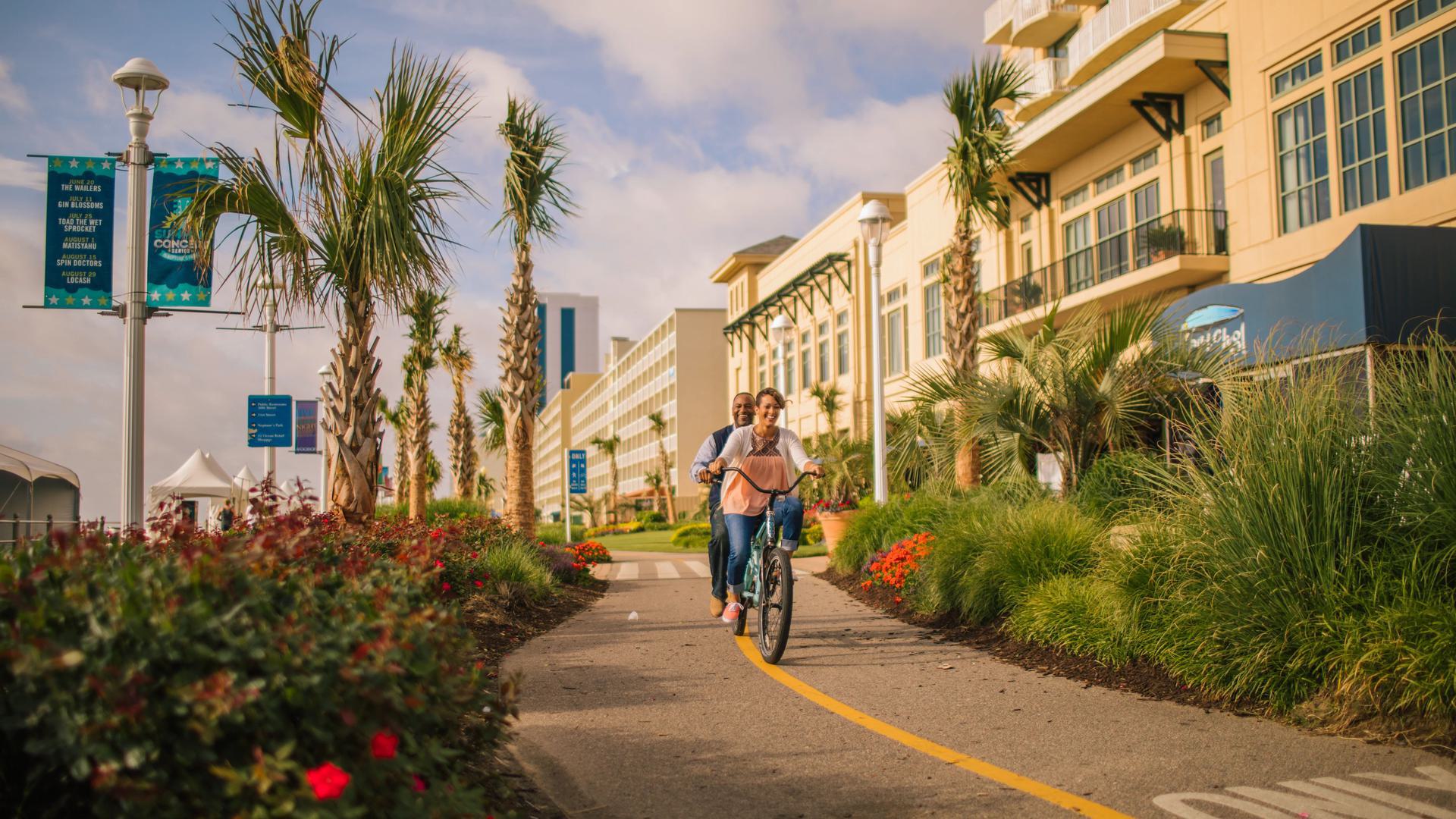 a photo of two people riding a bike on a bike path with palm trees around