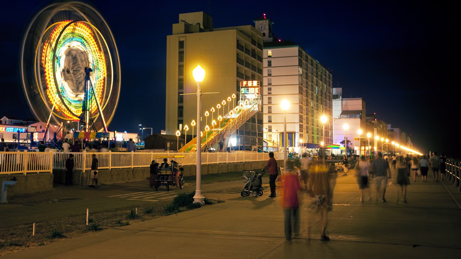 a photo of people on a boardwalk with a ride in the background and a building at night