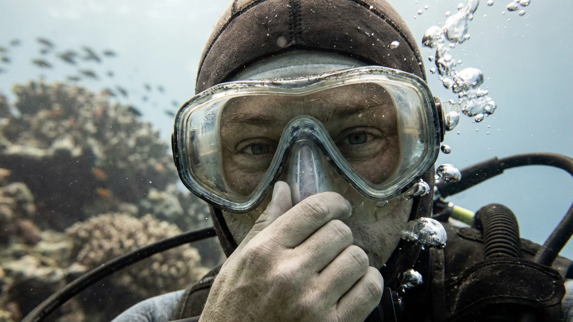 a man underwater in scuba gear holding his nose