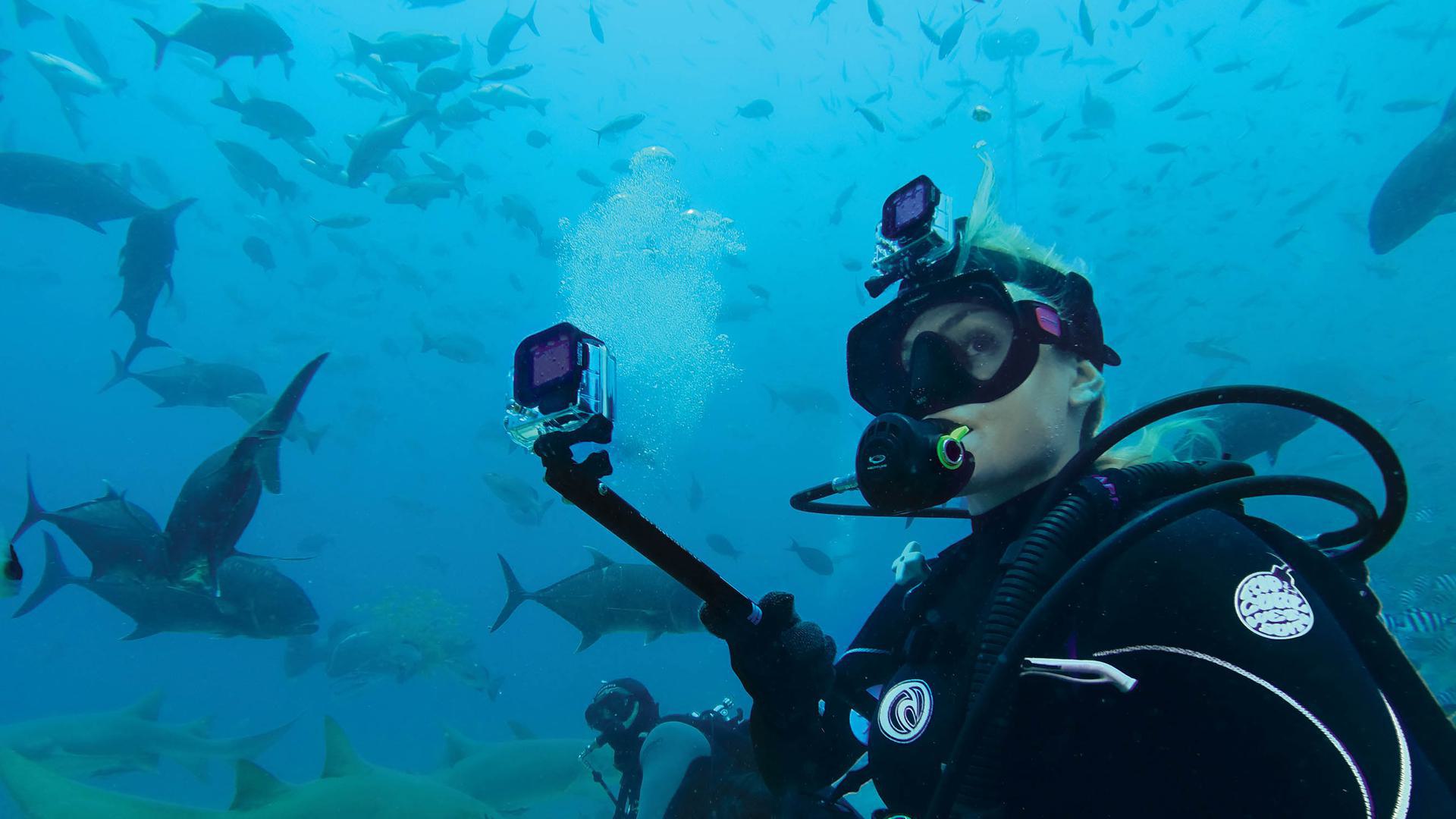 a man with a GoPro underwater with lots of fish