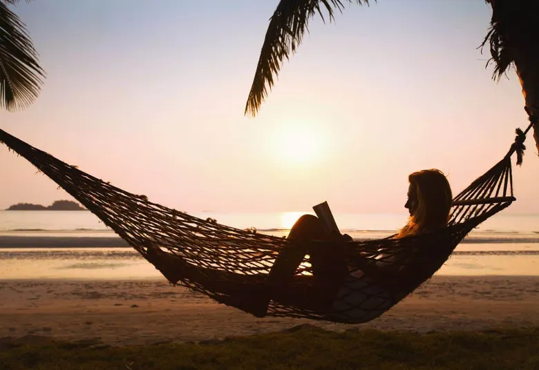 A person laying in a hammock reading a book on the beach