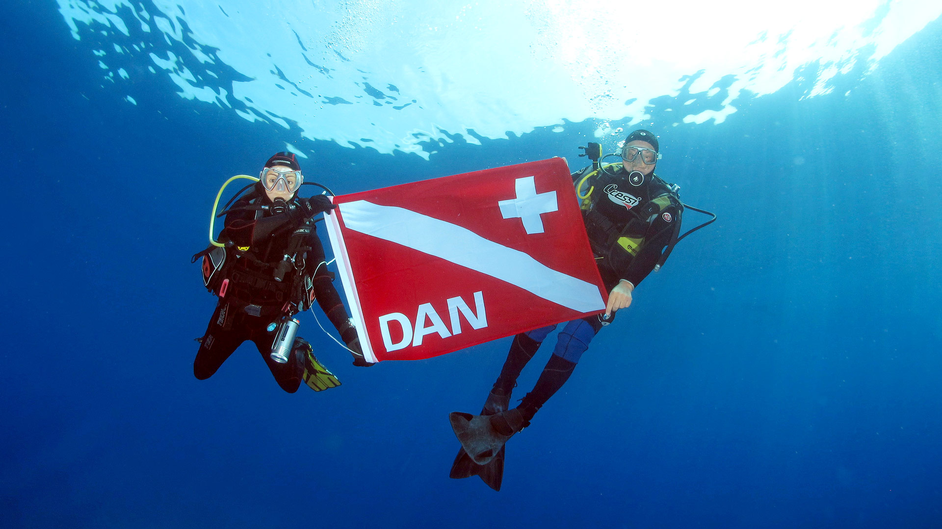 two underwater divers holding a DAN flag